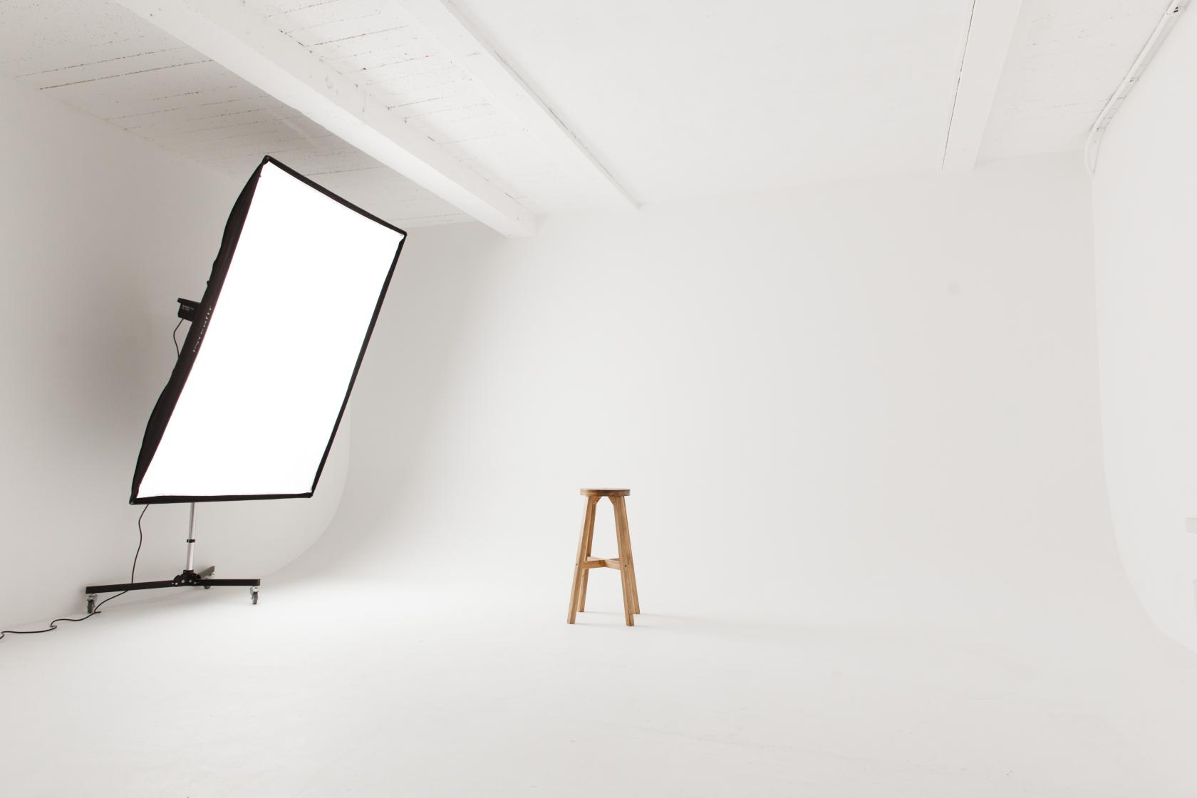 A photo studio with a seamless white cyclorama wall, large softbox light, and a wooden stool at Soif Studios.