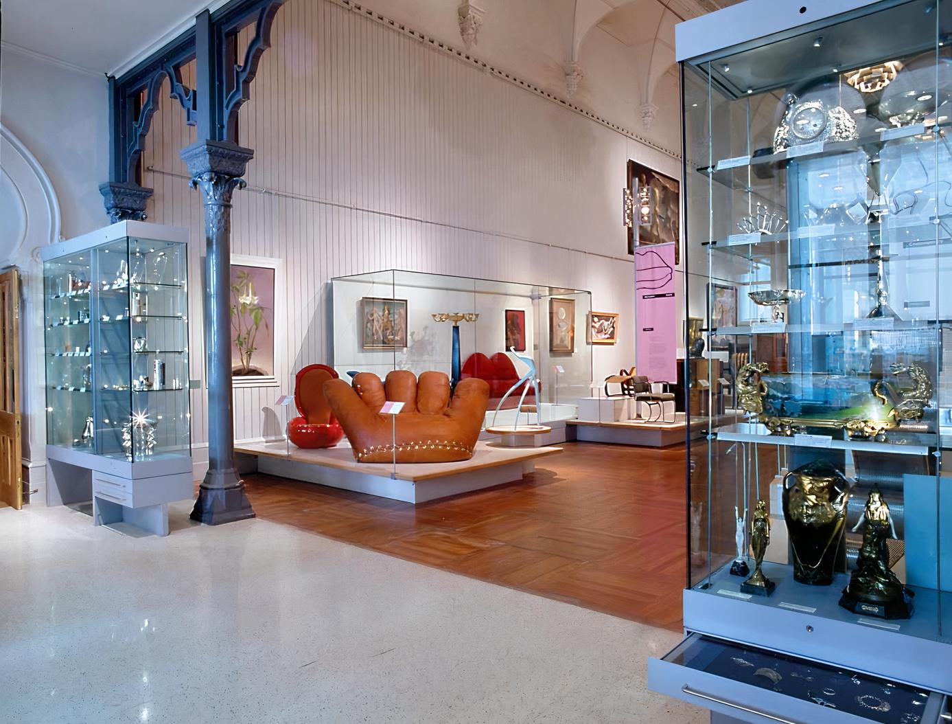 A museum gallery with glass display cases, decorative art pieces, and eclectic furniture at Brighton Museum & Art Gallery.
