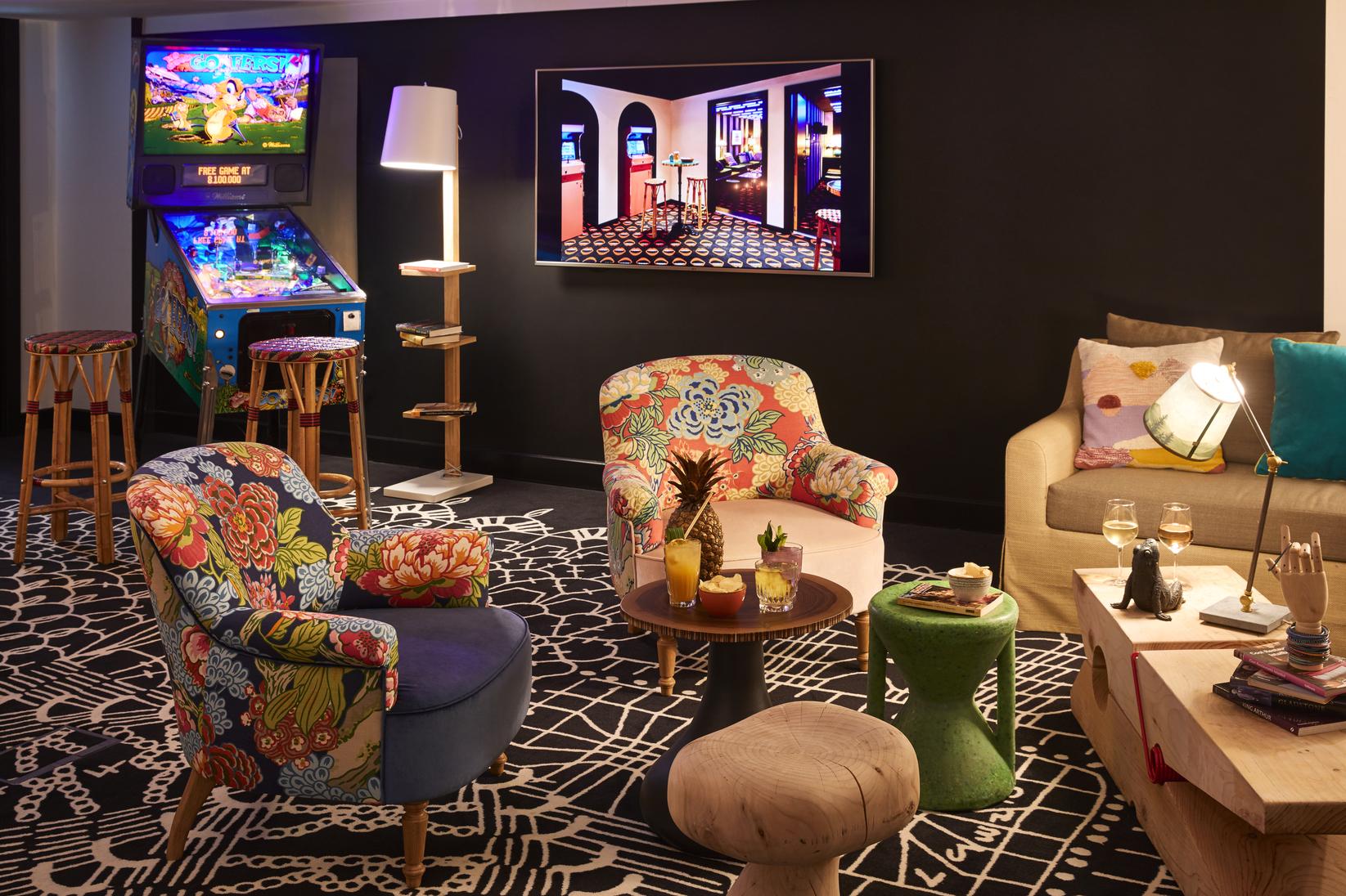 A hotel lounge with colorful patterned armchairs, arcade game machine, and eclectic decor at Mama Shelter London.