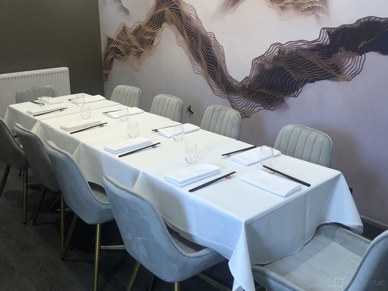 A dining room with a long table set with white linens, gray cushioned chairs, and abstract wall art at SINO Chinese Fine Dining.