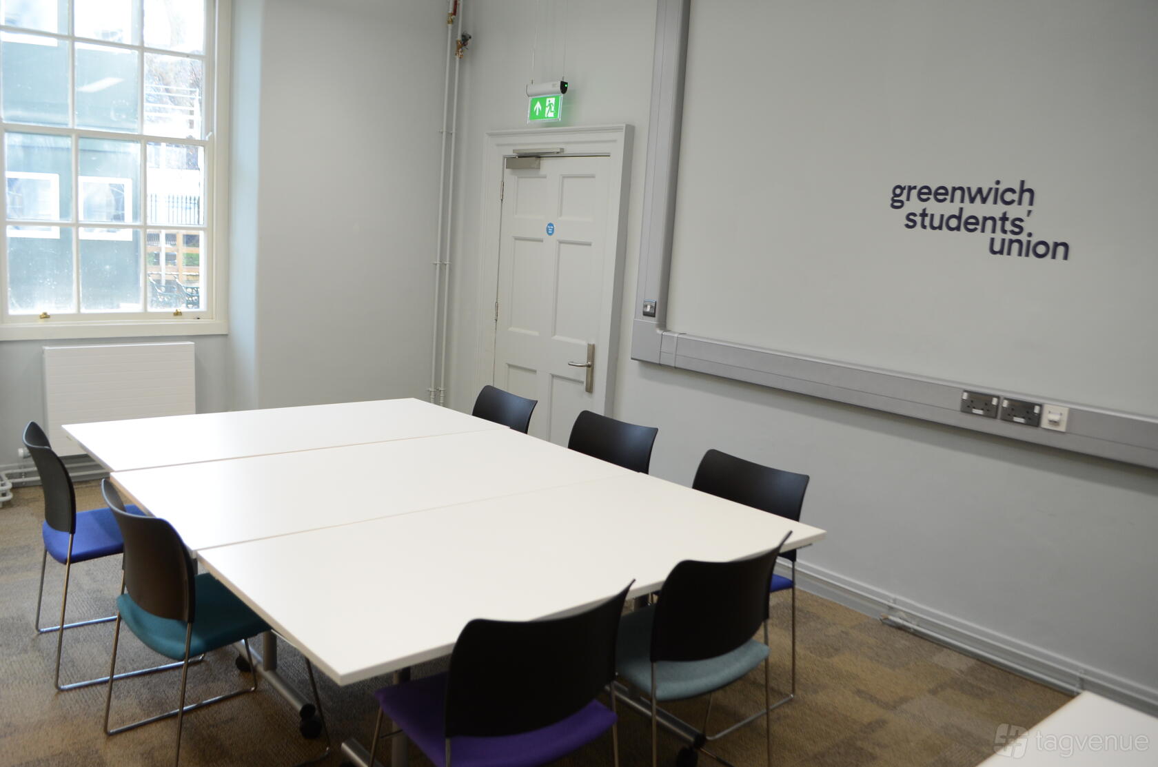 A meeting room with a rectangular table, black and purple chairs, large window, and whiteboard at Dreadnought Building.