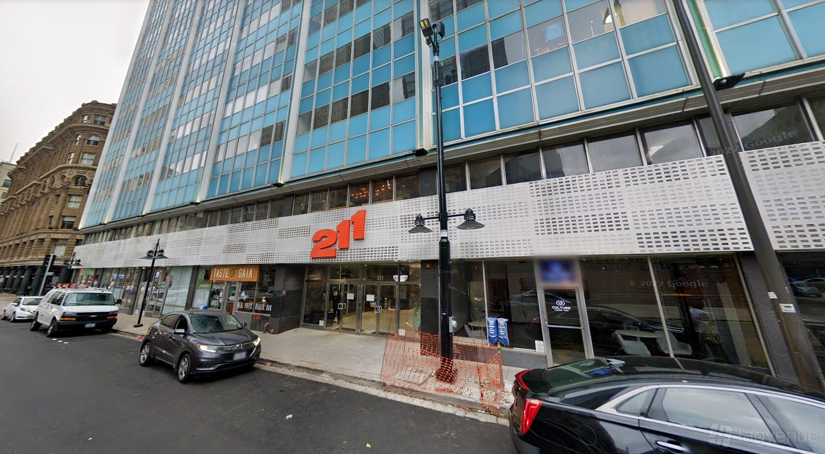 A glass-fronted office building with large windows, street-level entrance, and cars parked in front at Connected Coworking.