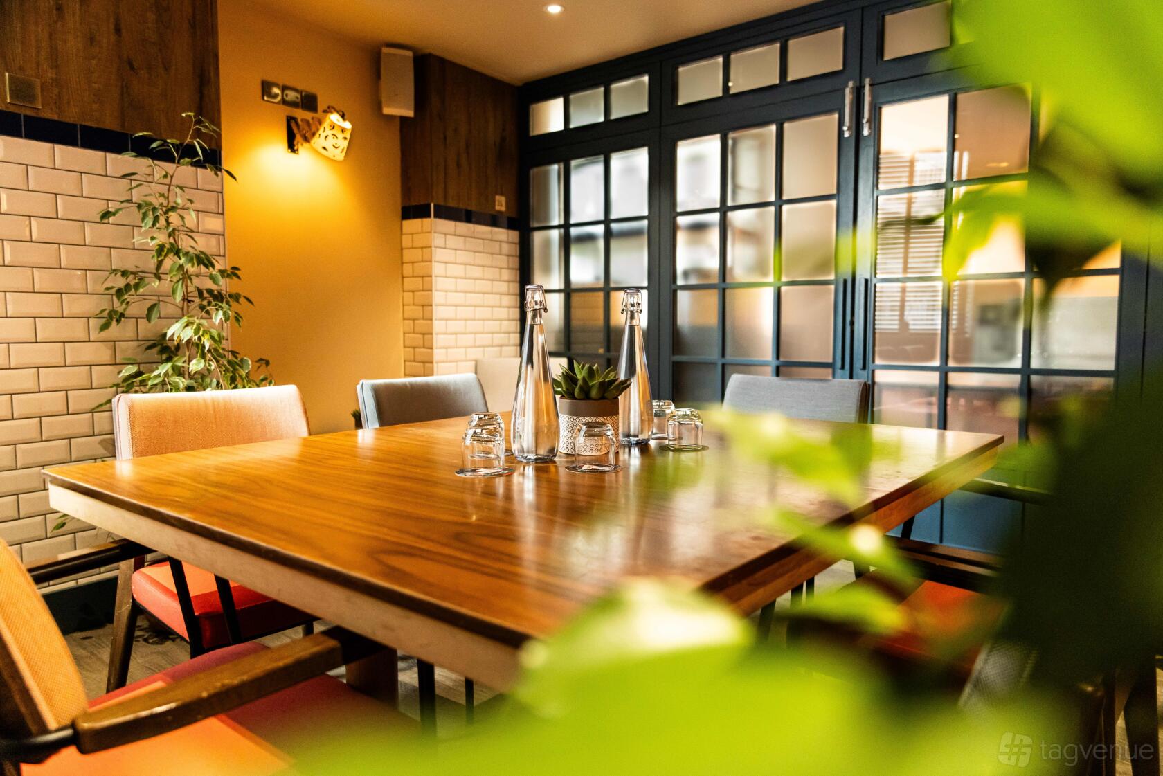 A hotel meeting room with a wooden table, glass water bottles, and natural light at The Corner London City.