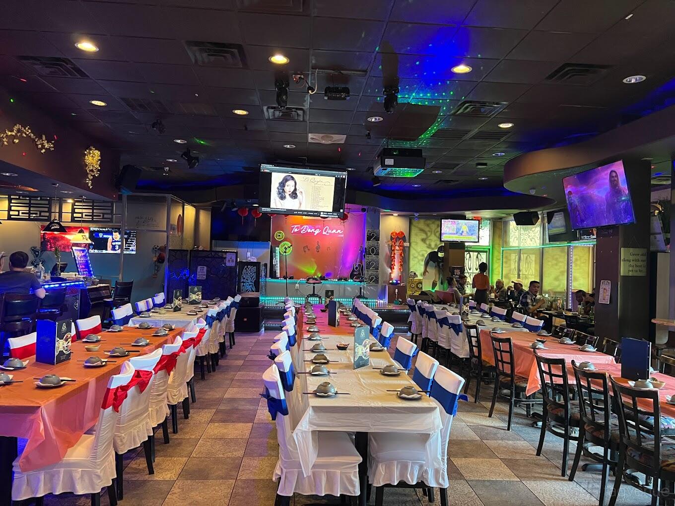 A restaurant with long banquet tables covered in red, white, and blue linens facing a stage at To Dong Restaurant.