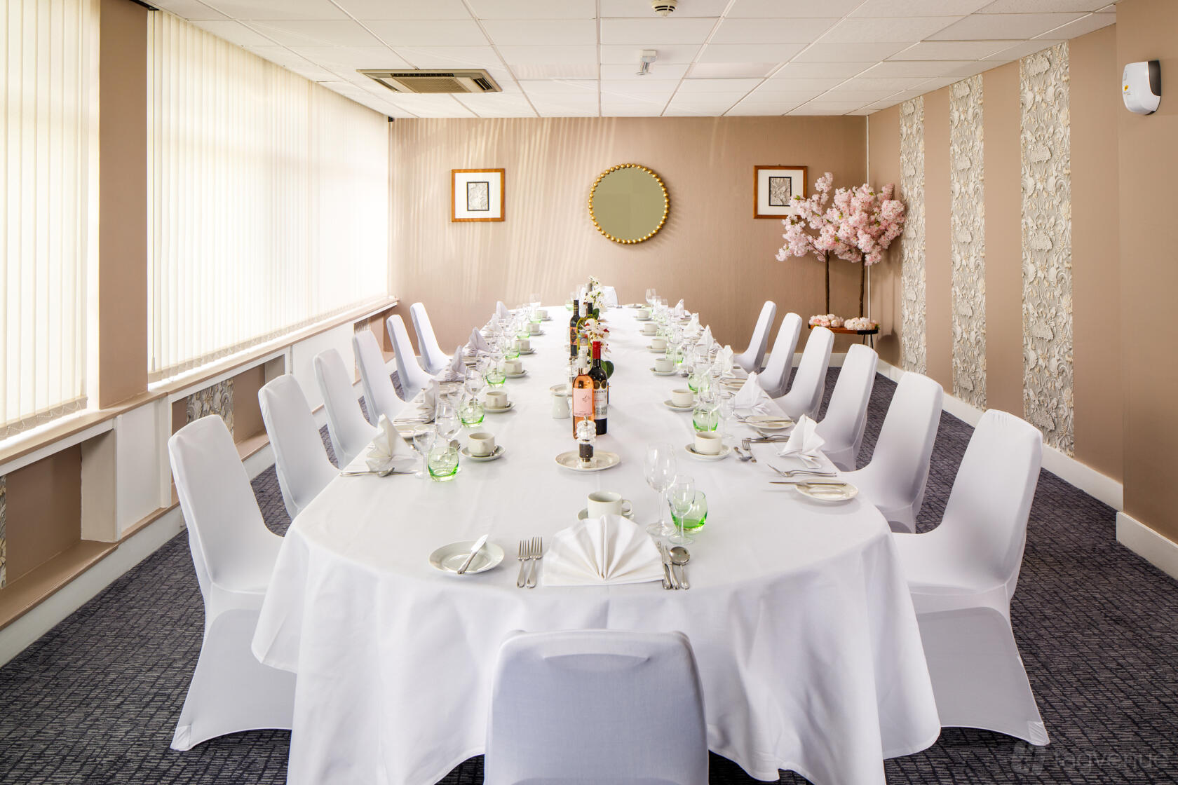 A meeting room with an oval table, white chair covers, and natural light at Harlow Hotel by Accor.