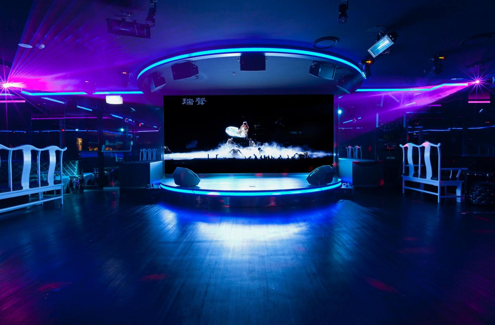 An event space in a karaoke bar with a large stage, LED lighting, and wall-mounted screen at Dynasty Karaoke.