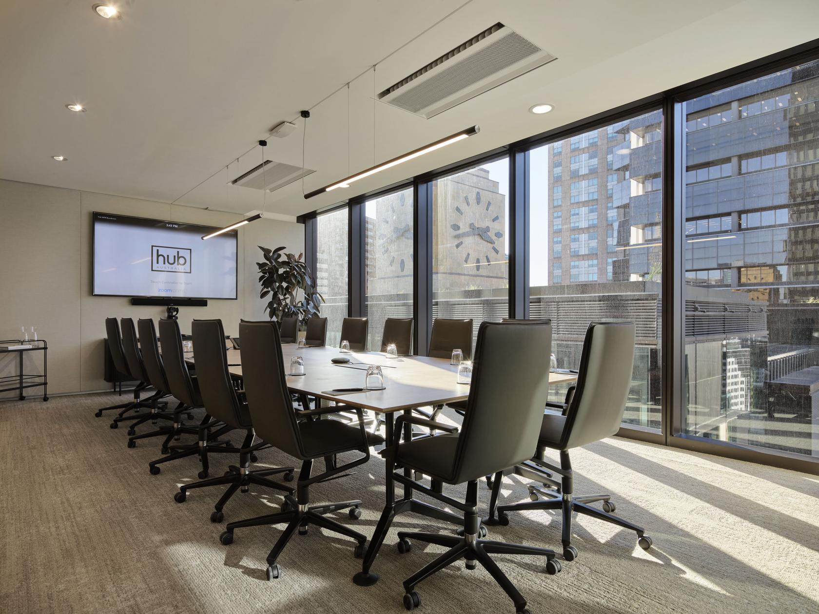 A boardroom in a coworking space with floor-to-ceiling windows, large meeting table, and wall-mounted screen at Hub Wynyard.