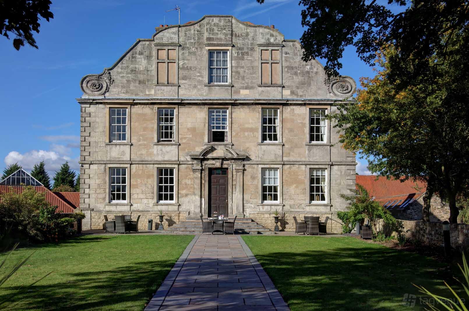 A historic hotel with a stone facade, symmetrical windows, and manicured lawn at Hellaby Hall Hotel.