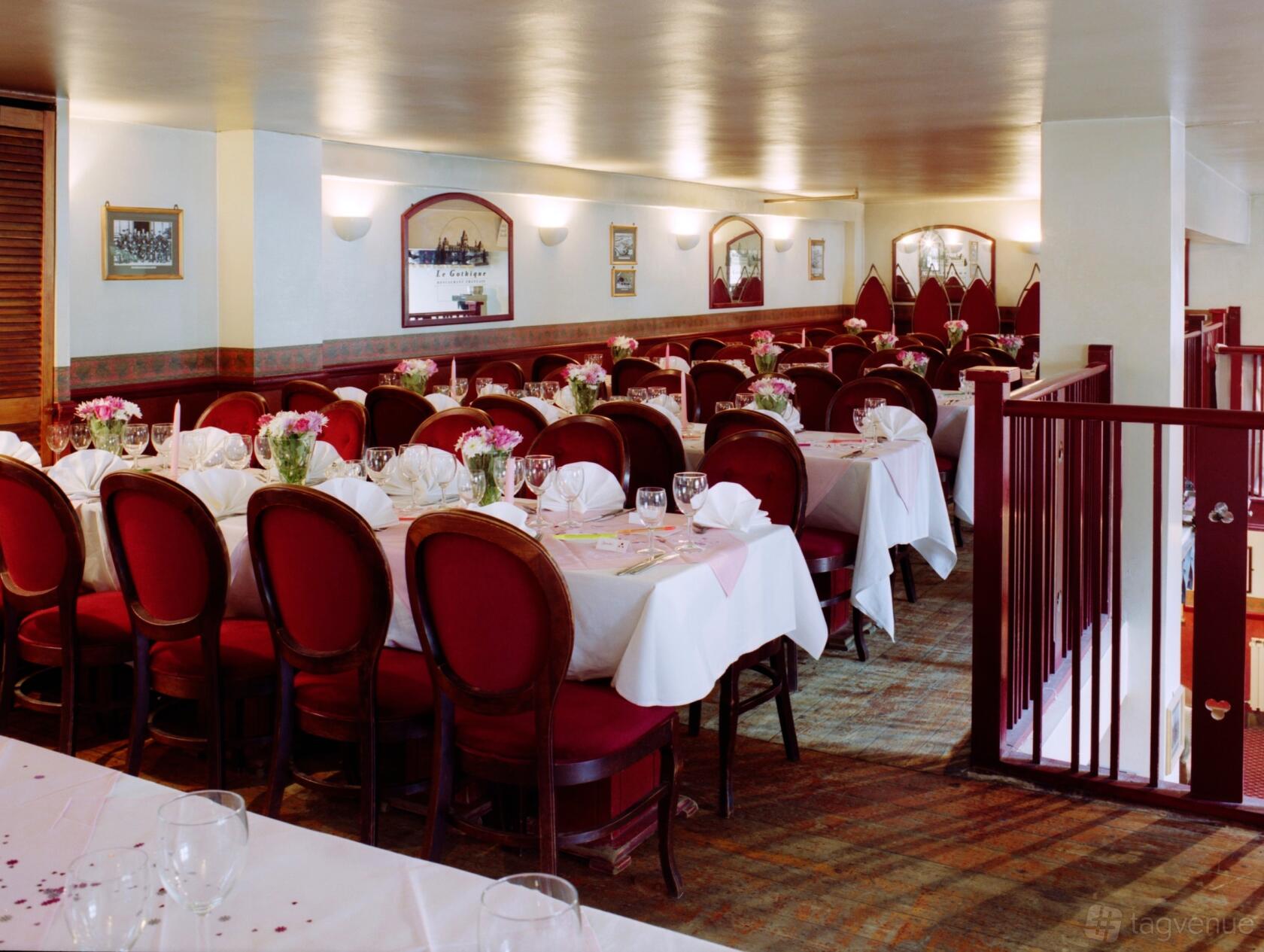 A restaurant banqueting hall with white-clothed tables, red upholstered chairs, and floral centerpieces at Le Gothique.