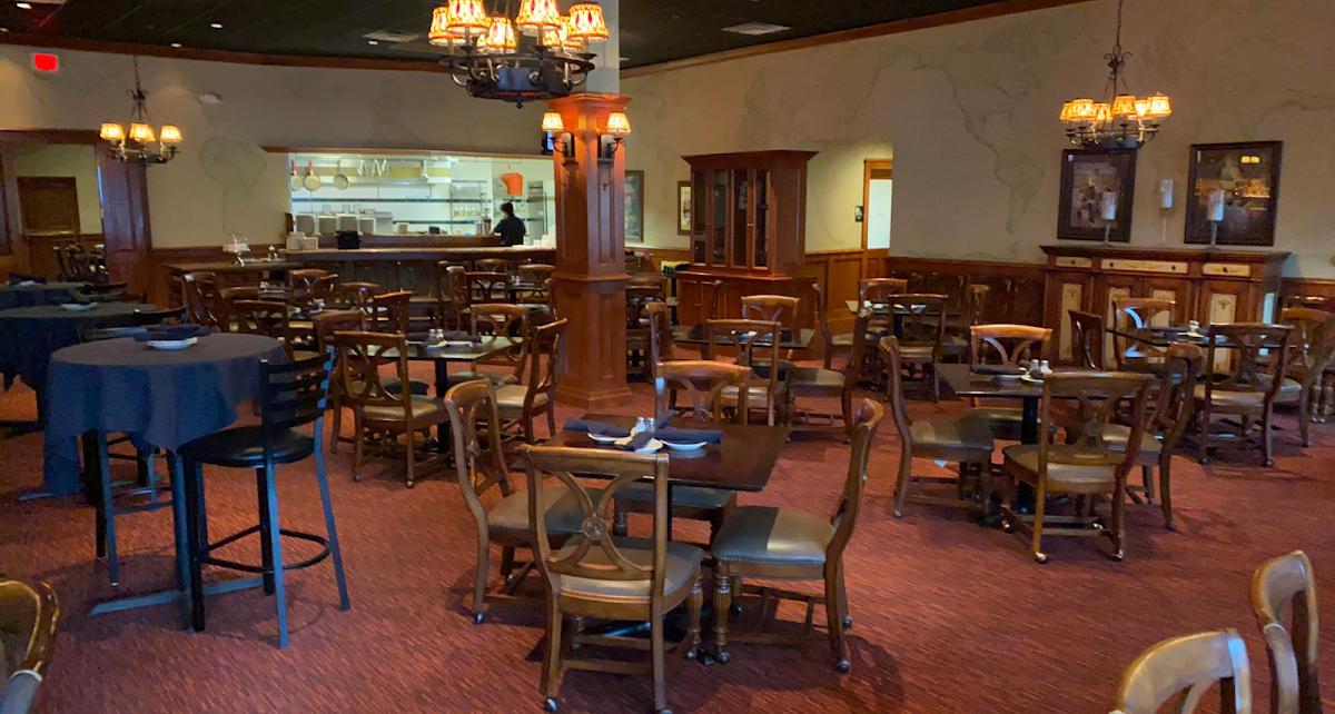 A pub with wooden tables and chairs, vintage light fixtures, and an open kitchen at Gillespie's Tavern at the Shire.