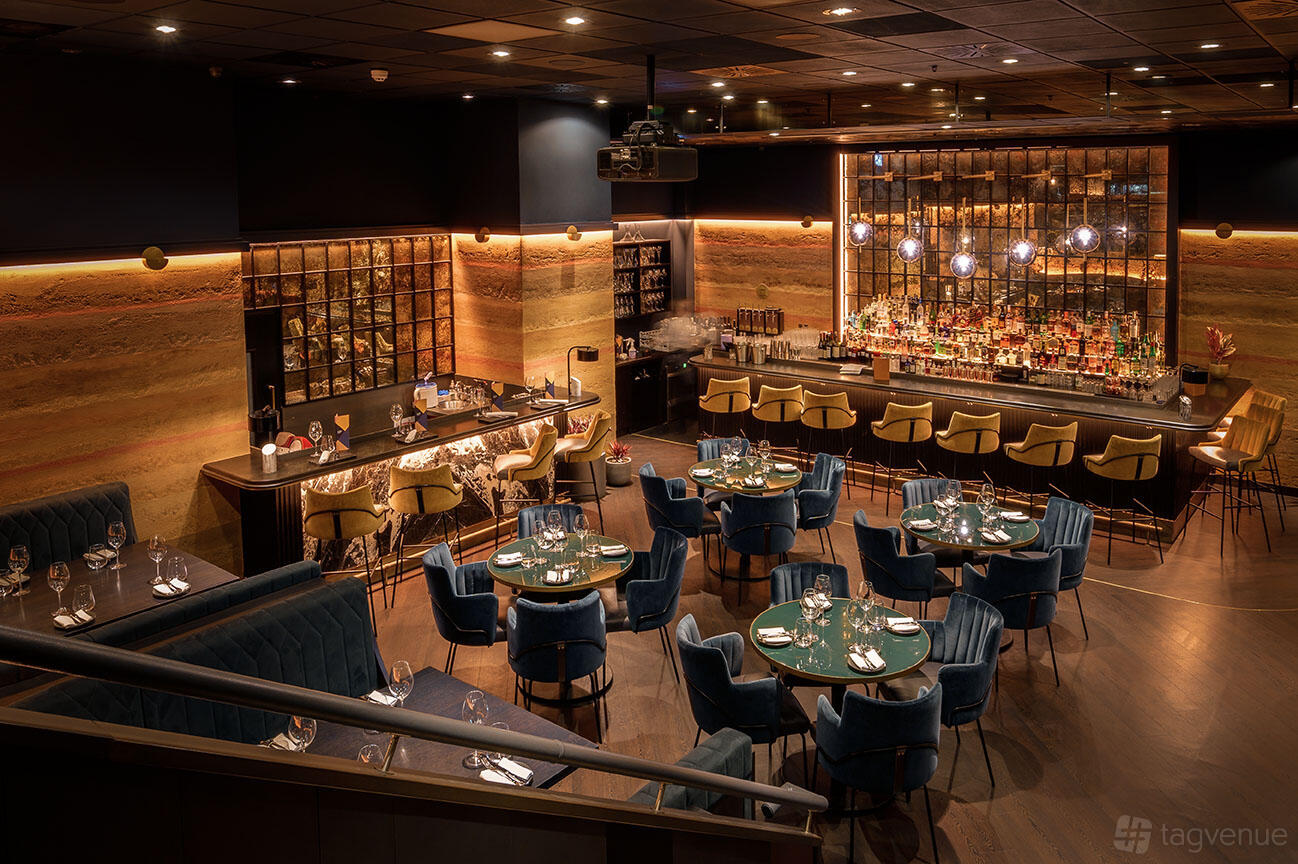 A restaurant with plush velvet seating, round tables, and a backlit marble bar at Gaucho Charlotte Street.