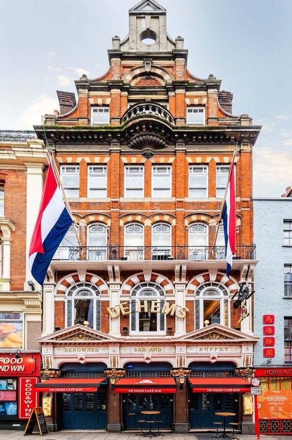 A pub with a red brick facade, arched windows, and Dutch flags at De Hems Pub.