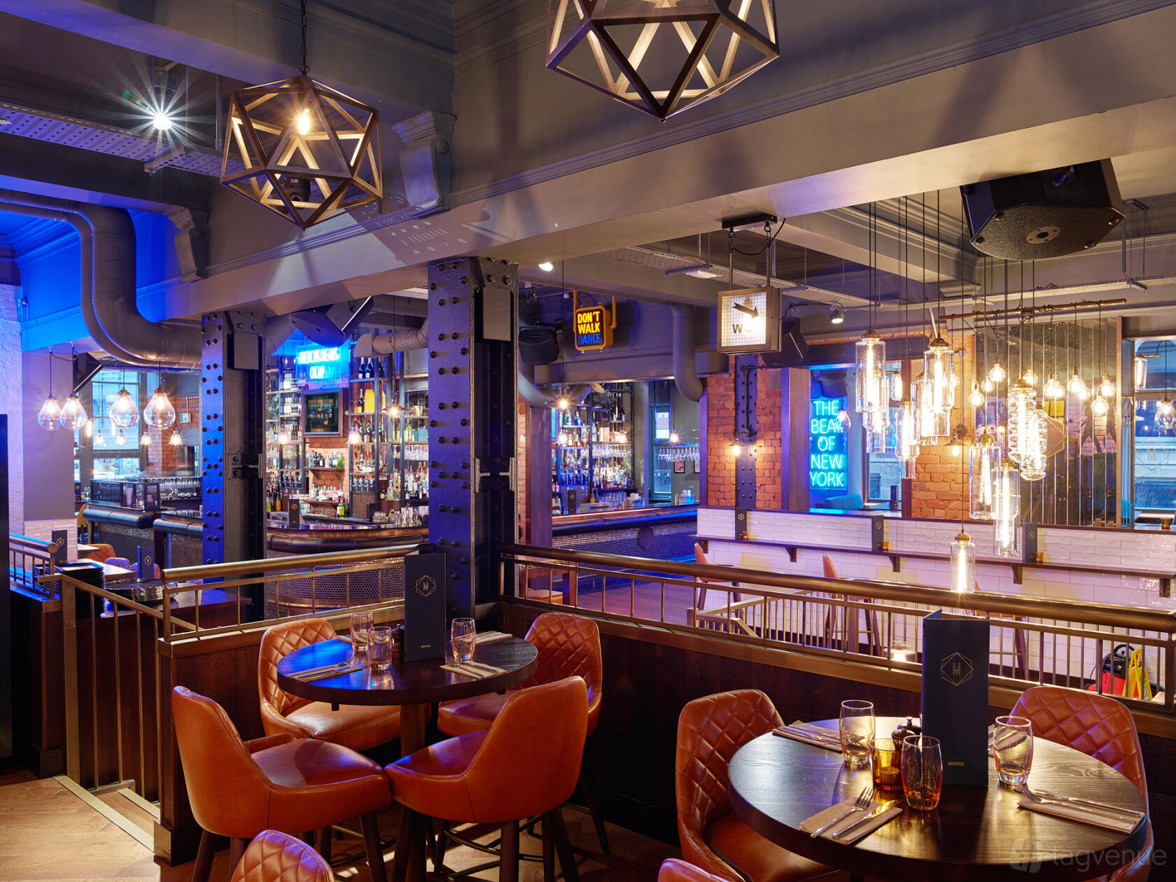A cocktail bar with leather seating, pendant lighting, and a neon sign at Manahatta Deansgate.