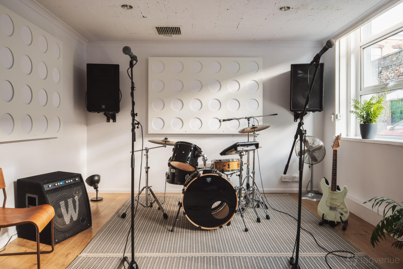 A rehearsal studio with a drum kit, microphones, amplifiers, and natural light at Factory Studios.
