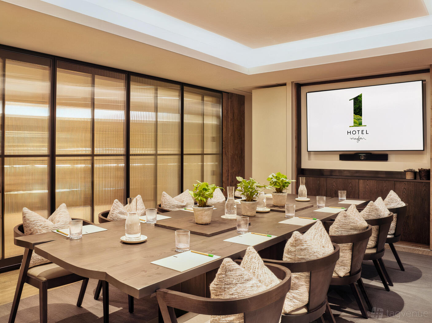 An event space with a wooden conference table, potted plants, cushioned chairs, and a large screen at 1 Hotel Mayfair.