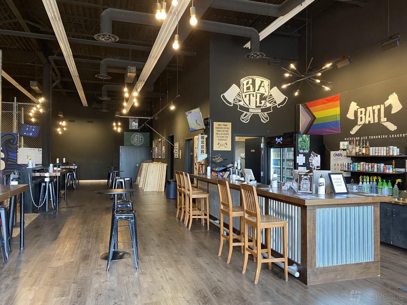 A bar with high-top tables, wooden stools, exposed ductwork, and axe-throwing lanes at BATL Grounds Vaughan.
