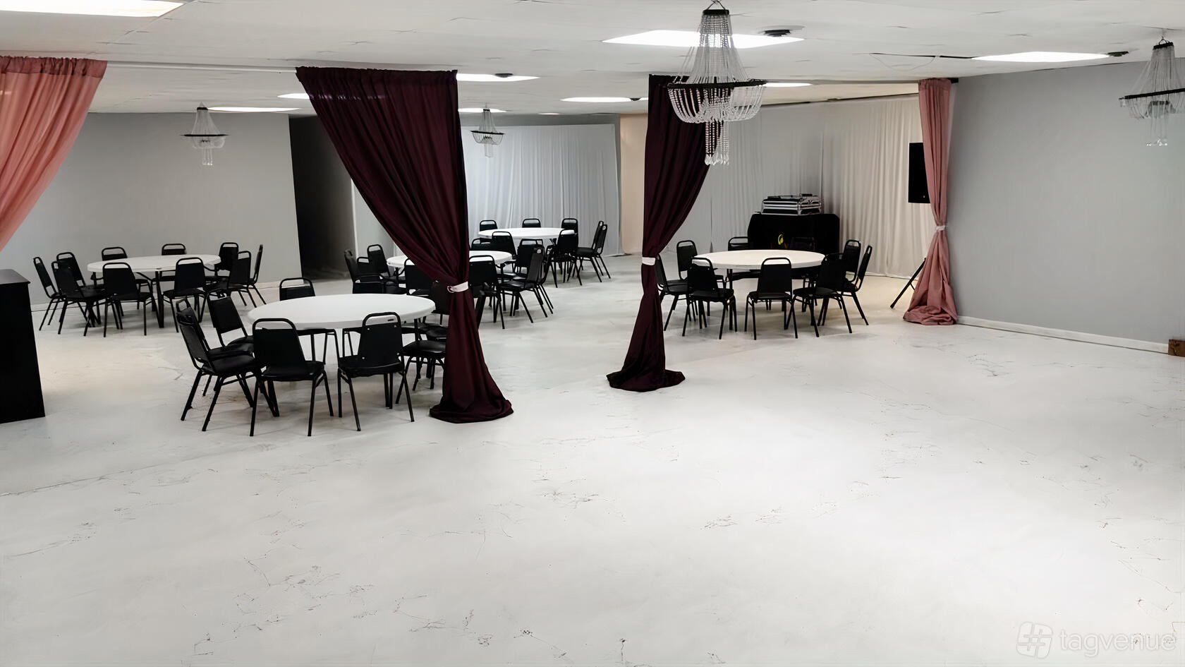 An event venue with round tables, black chairs, burgundy curtains, and chandeliers at Cozy Corner.