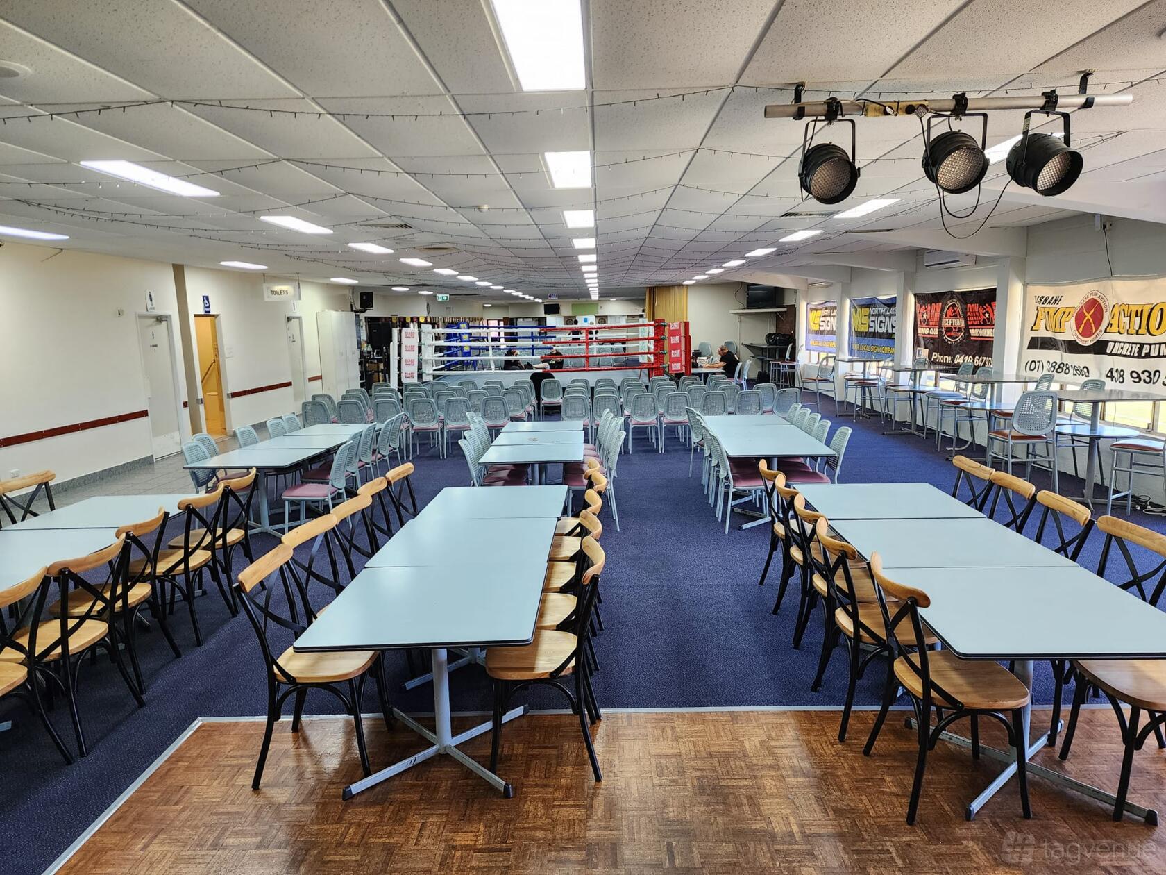 An event venue with rectangular tables, folding chairs, and a raised boxing ring at The Deception Bay Club.