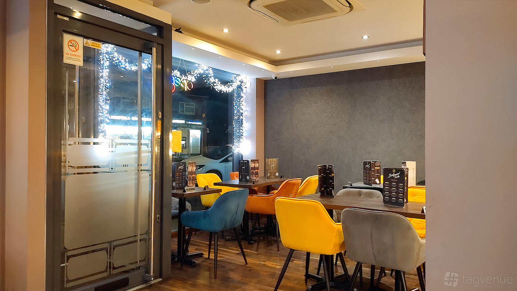 A restaurant interior with colorful upholstered chairs, wood floors, and wall lighting at Bollywood Tadka Indian Restaurant.