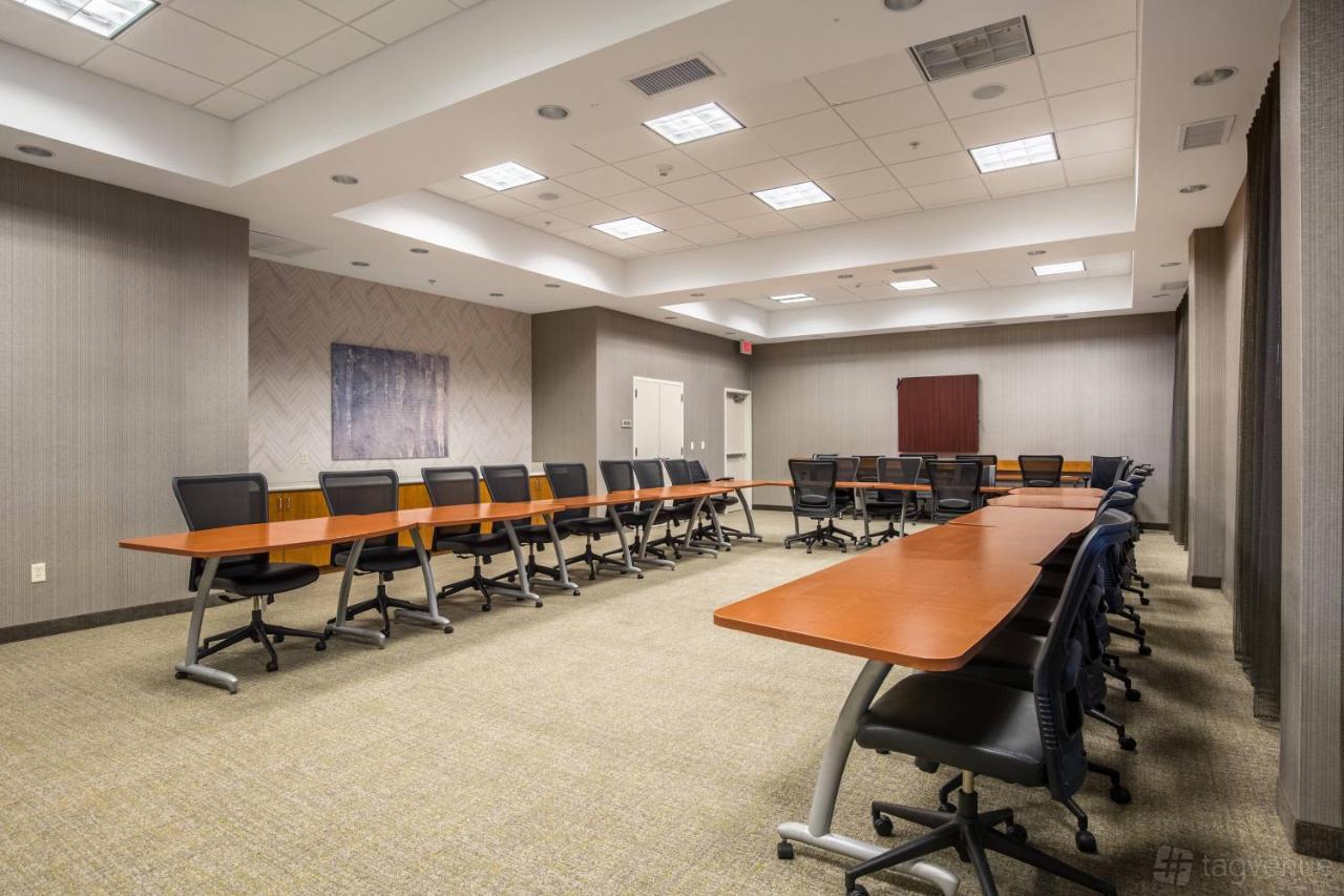 A hotel meeting room with U-shaped wooden tables, ergonomic chairs, and neutral gray walls at SpringHill Suites.