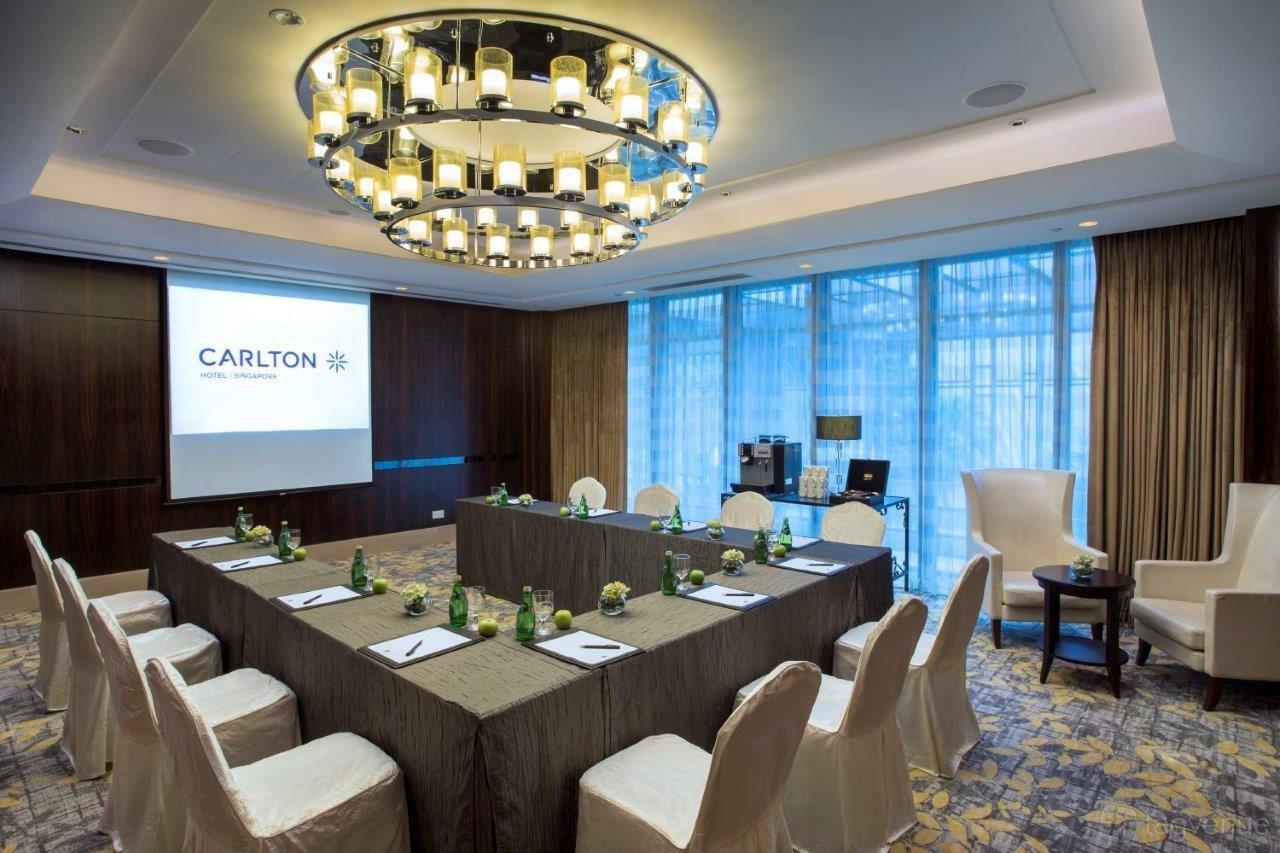 A function room with a U-shaped conference table, large chandelier, and floor-to-ceiling windows at Carlton Hotel Singapore.