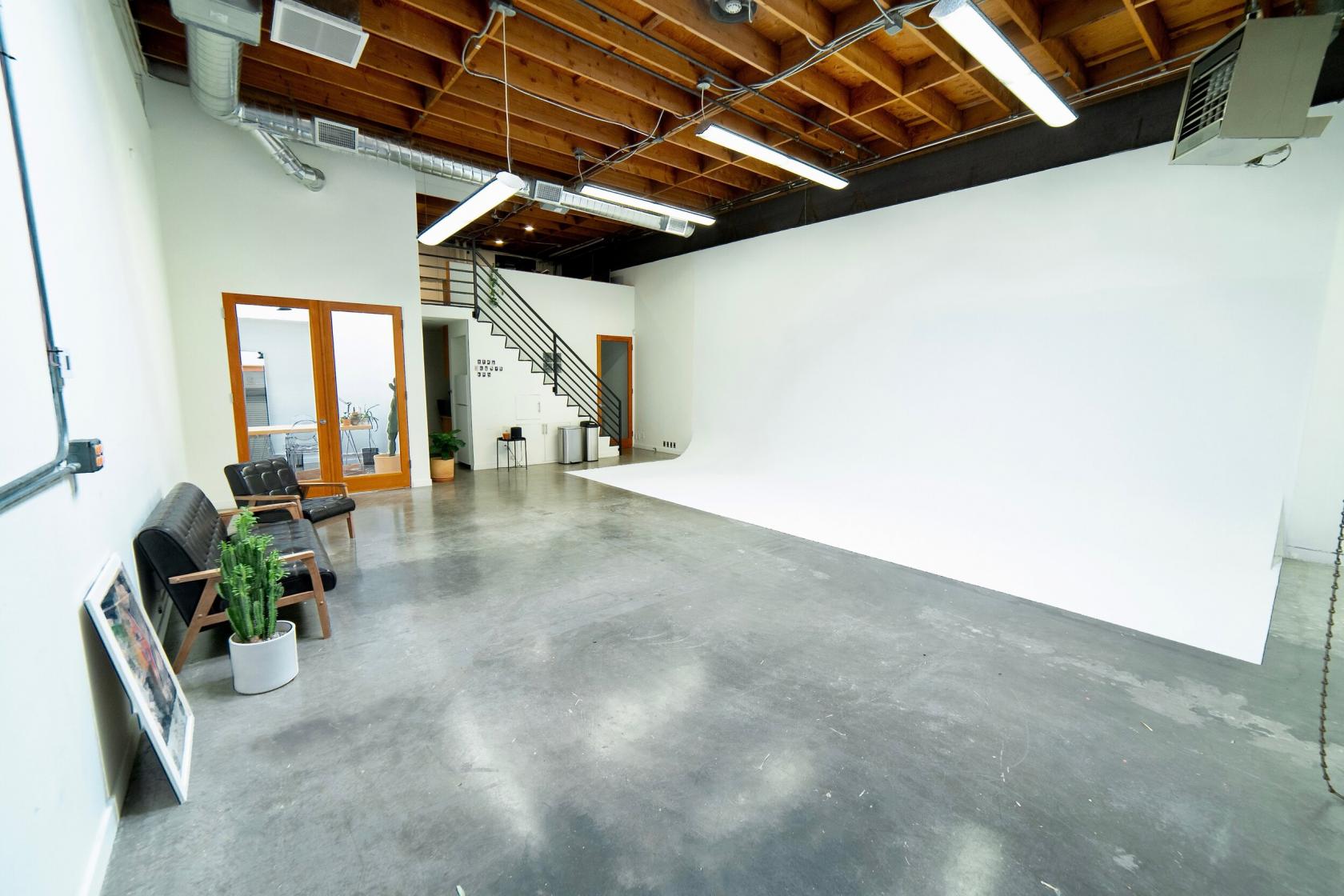A photo studio with a white cyclorama wall, polished concrete floor, and exposed wooden ceiling at ALT Studio.