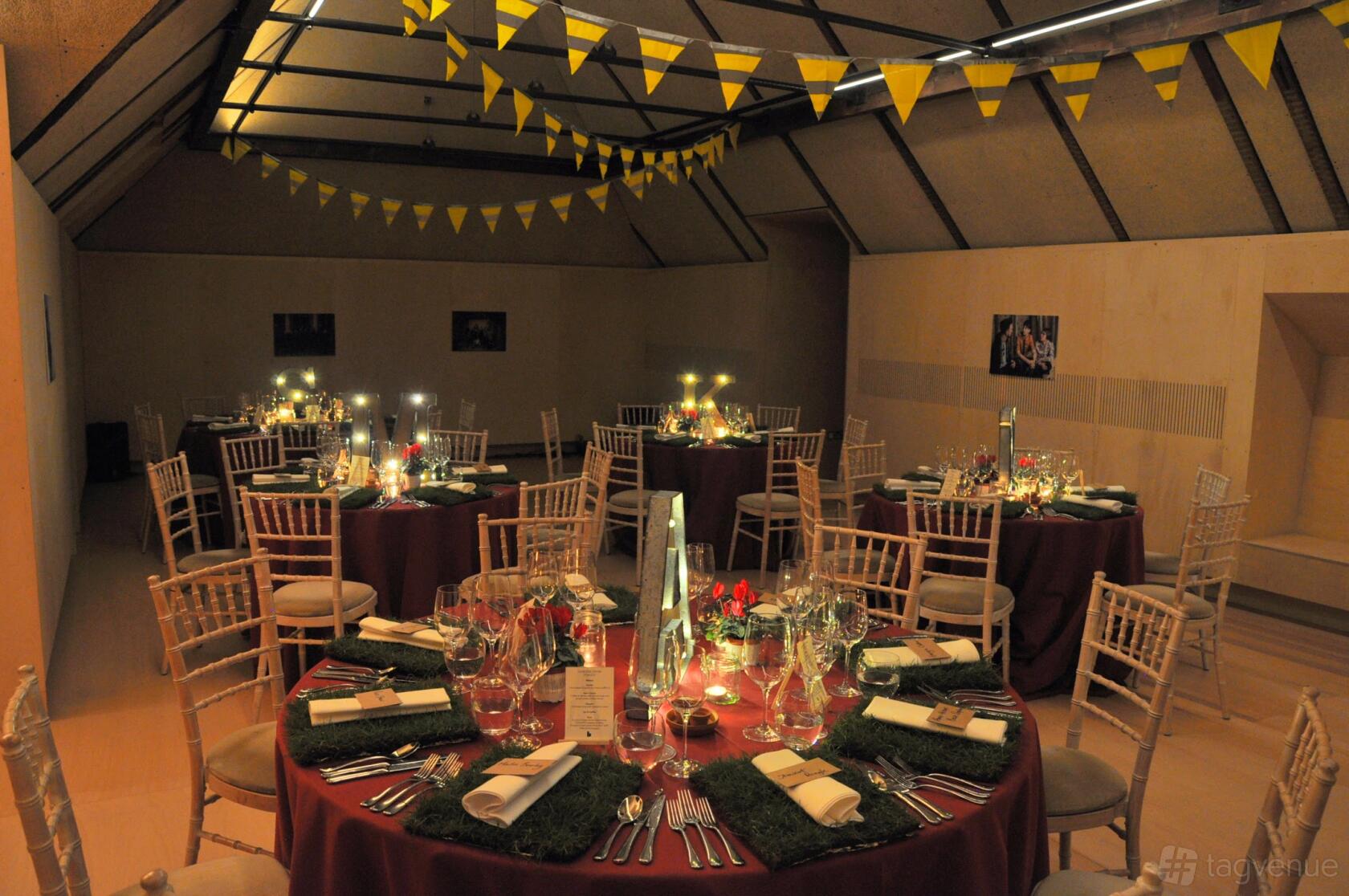 A rehearsal room with round tables set for dining, ambient lighting, and yellow bunting at Bush Theatre.