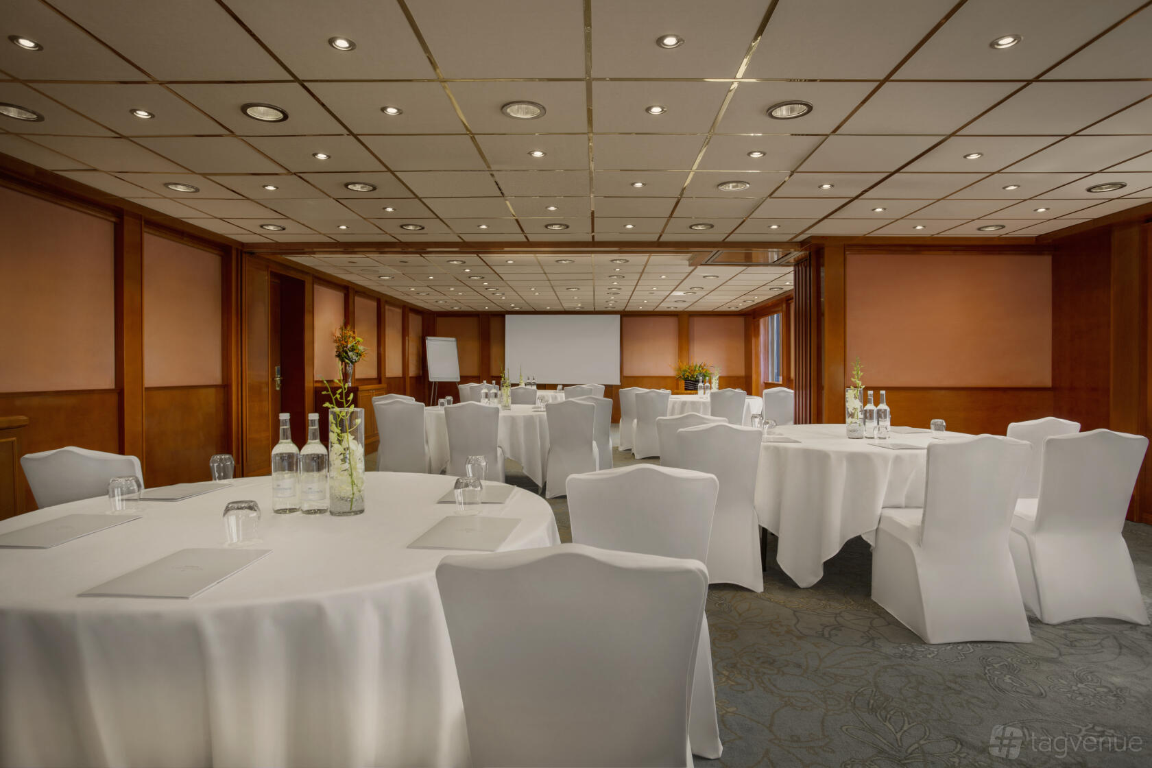 An event space in a restaurant with round tables draped in white linens and wood-paneled walls at Sunborn London Yacht Hotel.