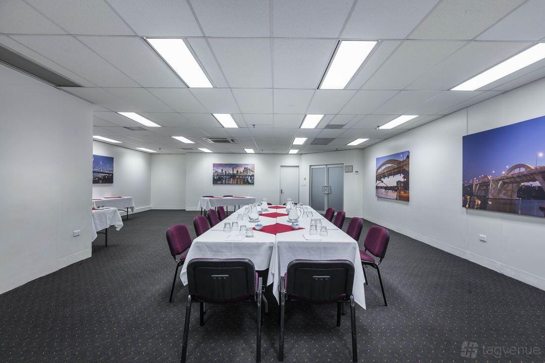 An auditorium with U-shaped tables, purple chairs, carpeted floor, and framed city photos at George Williams Hotel.