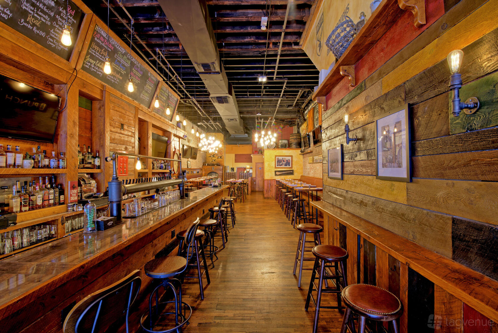 An event space in a cocktail bar with a long wooden bar counter, exposed bulb lighting, and high stools at Monk McGinn's.