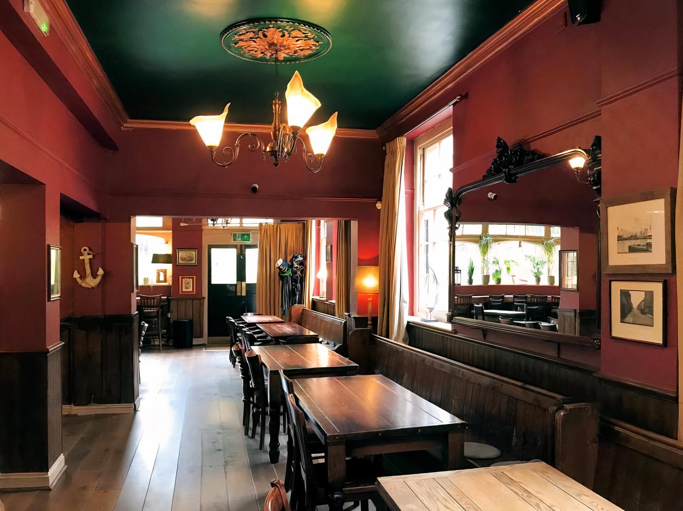 A pub with red walls, wooden tables, wall art, a large mirror, and natural light at The Ship & Whale.
