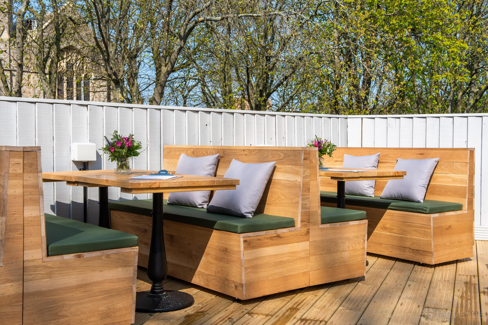An outdoor pub area with wooden booths, green seat cushions, and potted flowers on tables at The Park View.