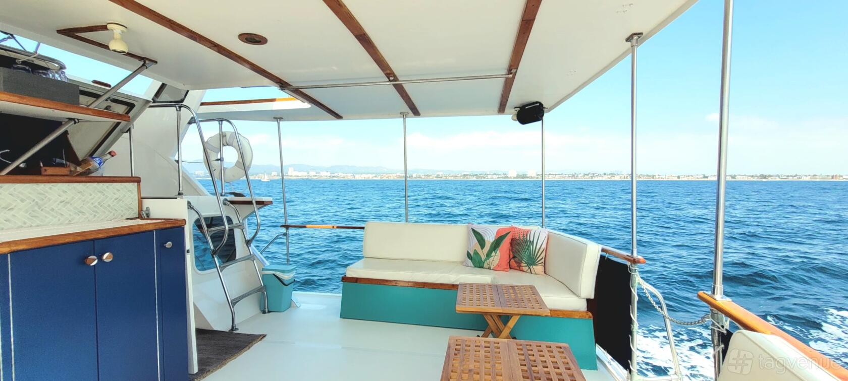 A yacht deck with cushioned seating, wooden tables, and ocean views on the Calico Yacht Charter.