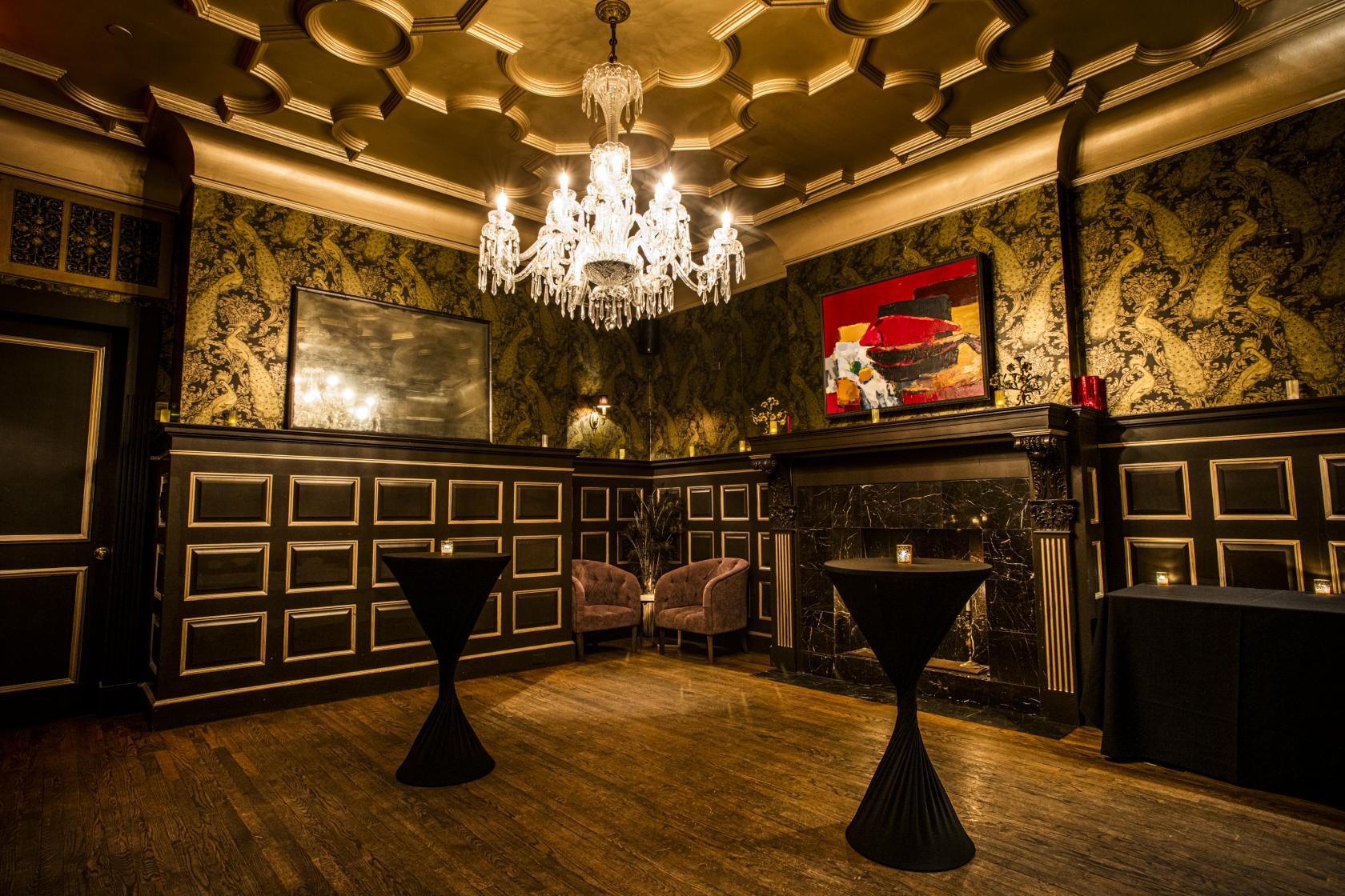 A function room with a chandelier, patterned wallpaper, and two cocktail tables at The Raines Law Room at The William.