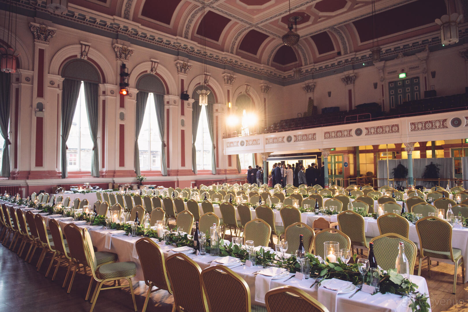 An event venue with long banquet tables, green chairs, arched windows, and a vaulted ceiling at Victoria Hall Saltaire.