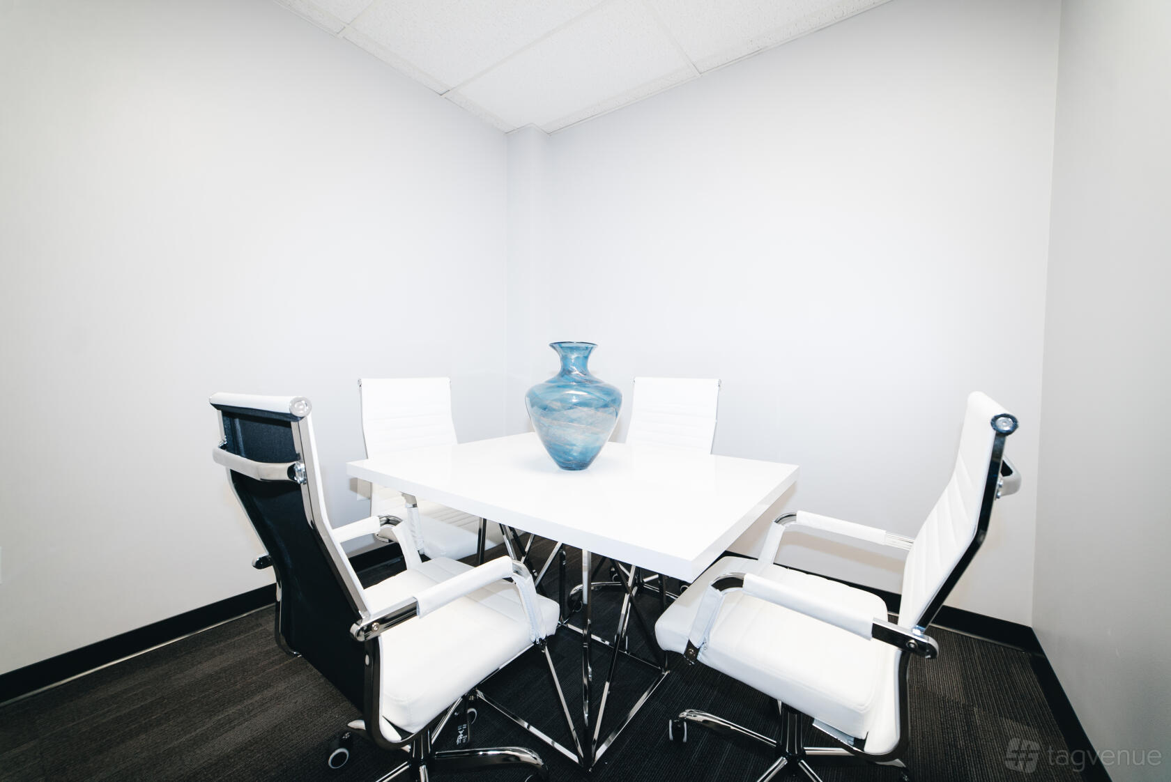 A meeting room with a white square table, four white office chairs, and a large blue vase at Perfect Office Solutions - Alexandria.