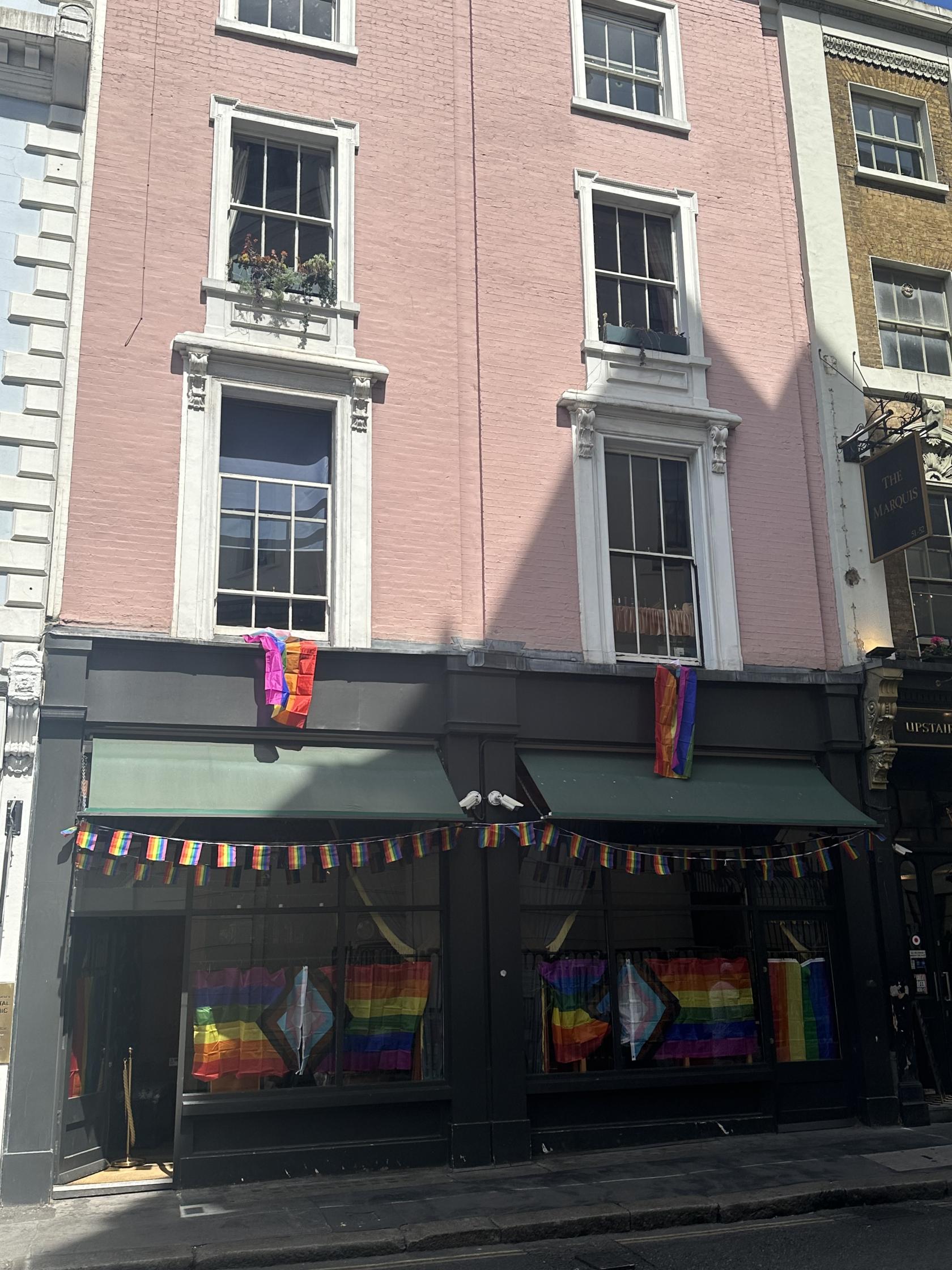 A pink building exterior with green awnings and rainbow flags displayed at Brydges Place Club.
