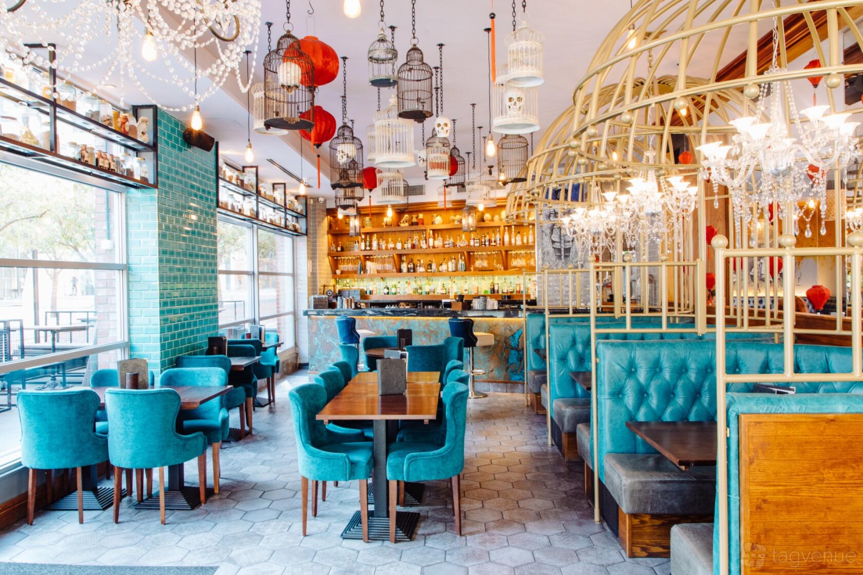 A restaurant with teal upholstered seating, hanging birdcages, and a well-stocked bar at Siamais.