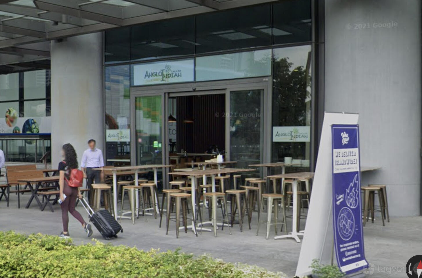A restaurant terrace with high wooden tables and stools under a covered area at Anglo Indian Cafe & Bar - Marina One.