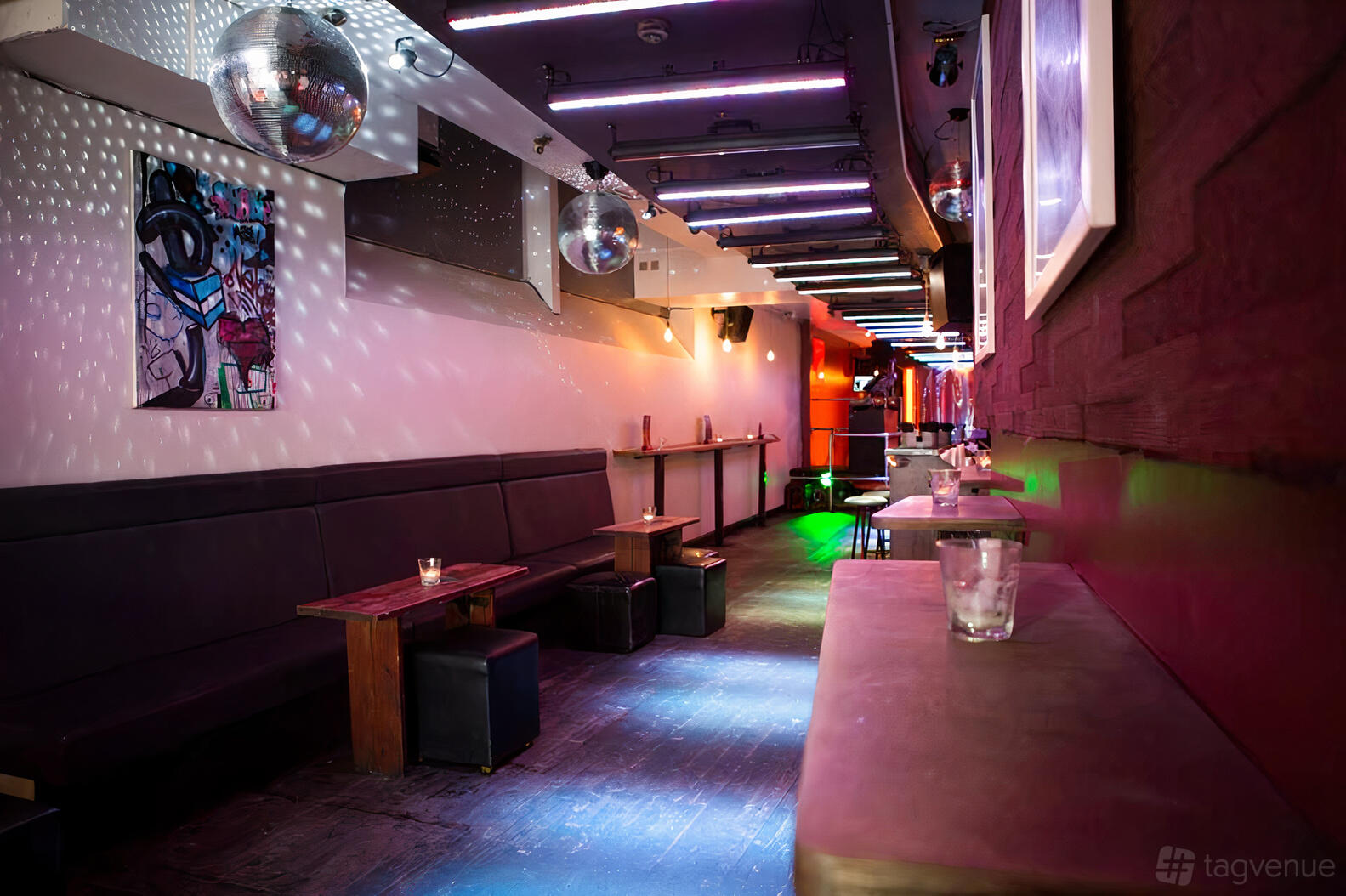 A bar with disco balls, LED ceiling lights, and bench seating with small wooden tables at Trafik.