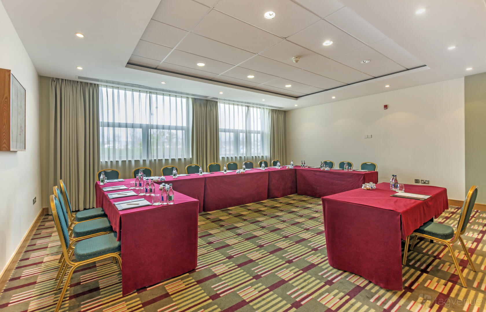 A meeting room with U-shaped tables covered in burgundy cloths, green chairs, and large windows at CityNorth Hotel & Conference Centre.