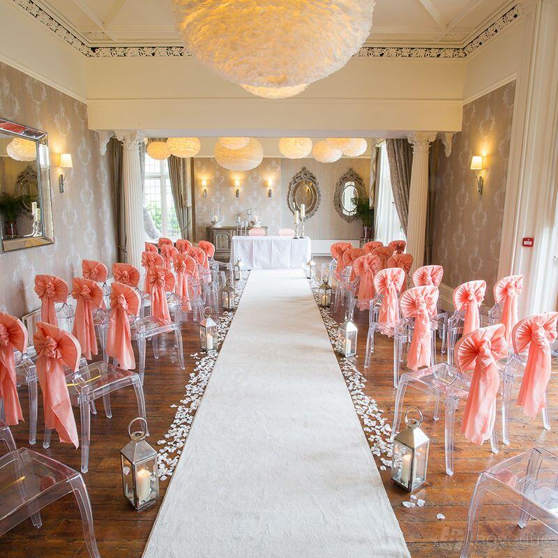 An event venue with clear chairs draped in pink sashes, white aisle runner, and lanterns at Falcon Manor.