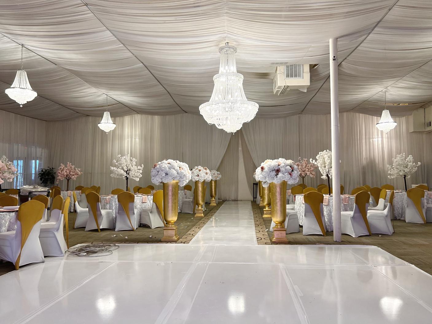 A banqueting hall with draped ceilings, crystal chandeliers, and gold vases with white floral arrangements at Bellagio Banquet Hall.