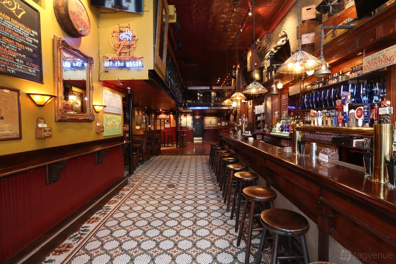 A bar with patterned tile flooring, a long wooden counter, bar stools, hanging lamps, and wall menus at Off the Wagon.
