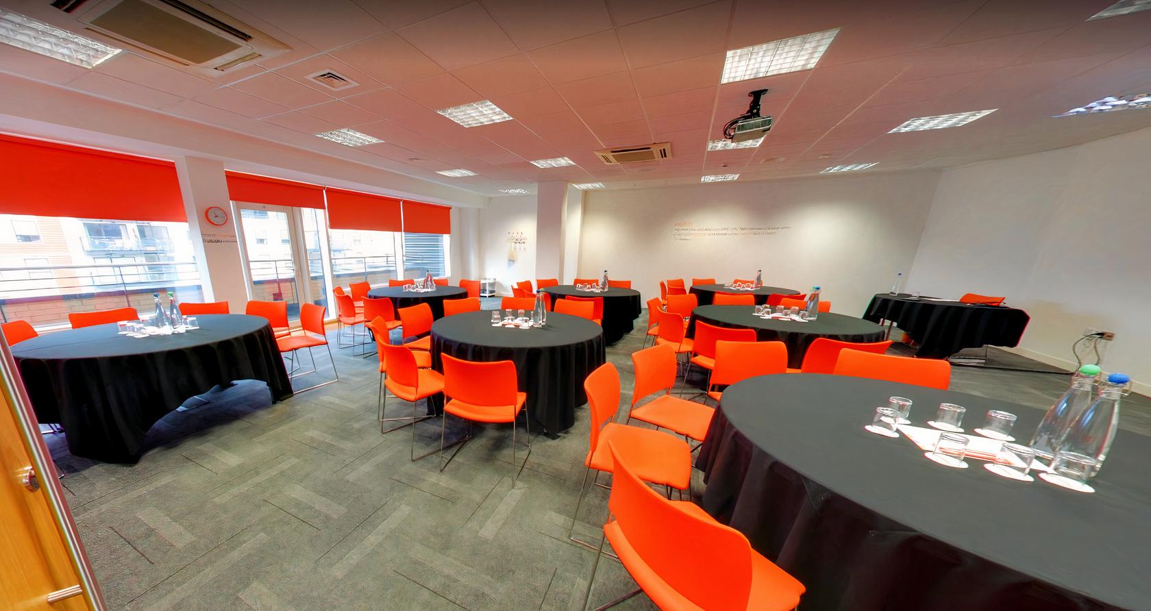 An event space with round tables covered in black linens and orange chairs at The Studio Leeds.