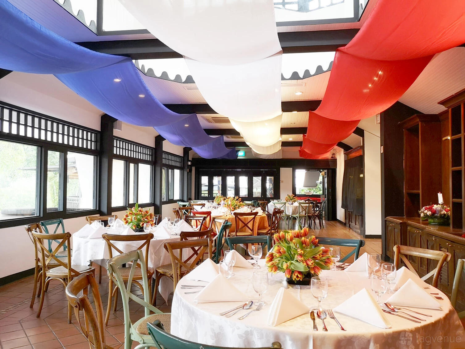 A bar with round tables set with white linens, floral centerpieces, and colorful fabric drapes at Hollandse Club.