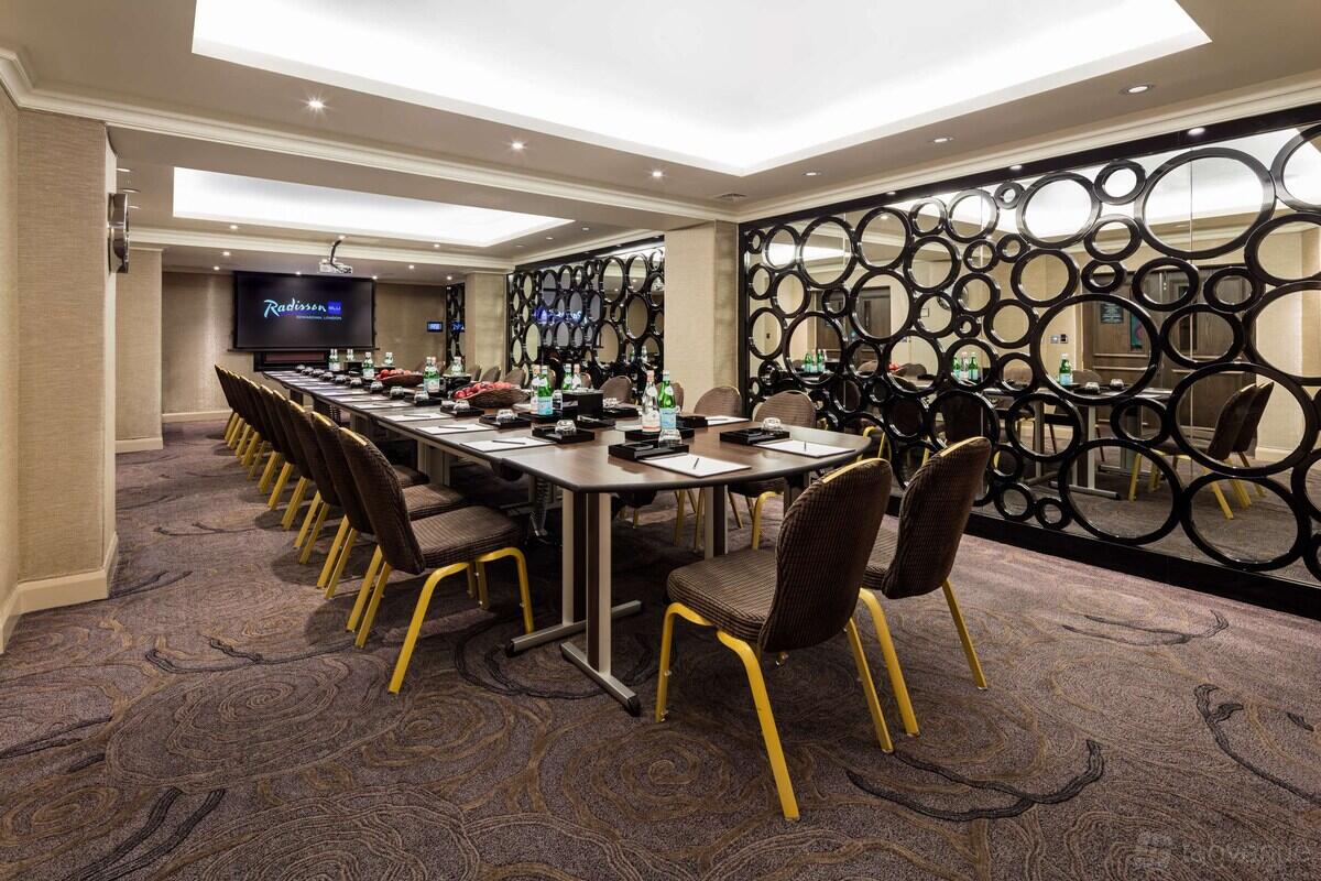 A meeting room with a long boardroom table, mirrored wall panels with circular patterns, and ceiling lights at Radisson Blu Hotel, London South Kensington.