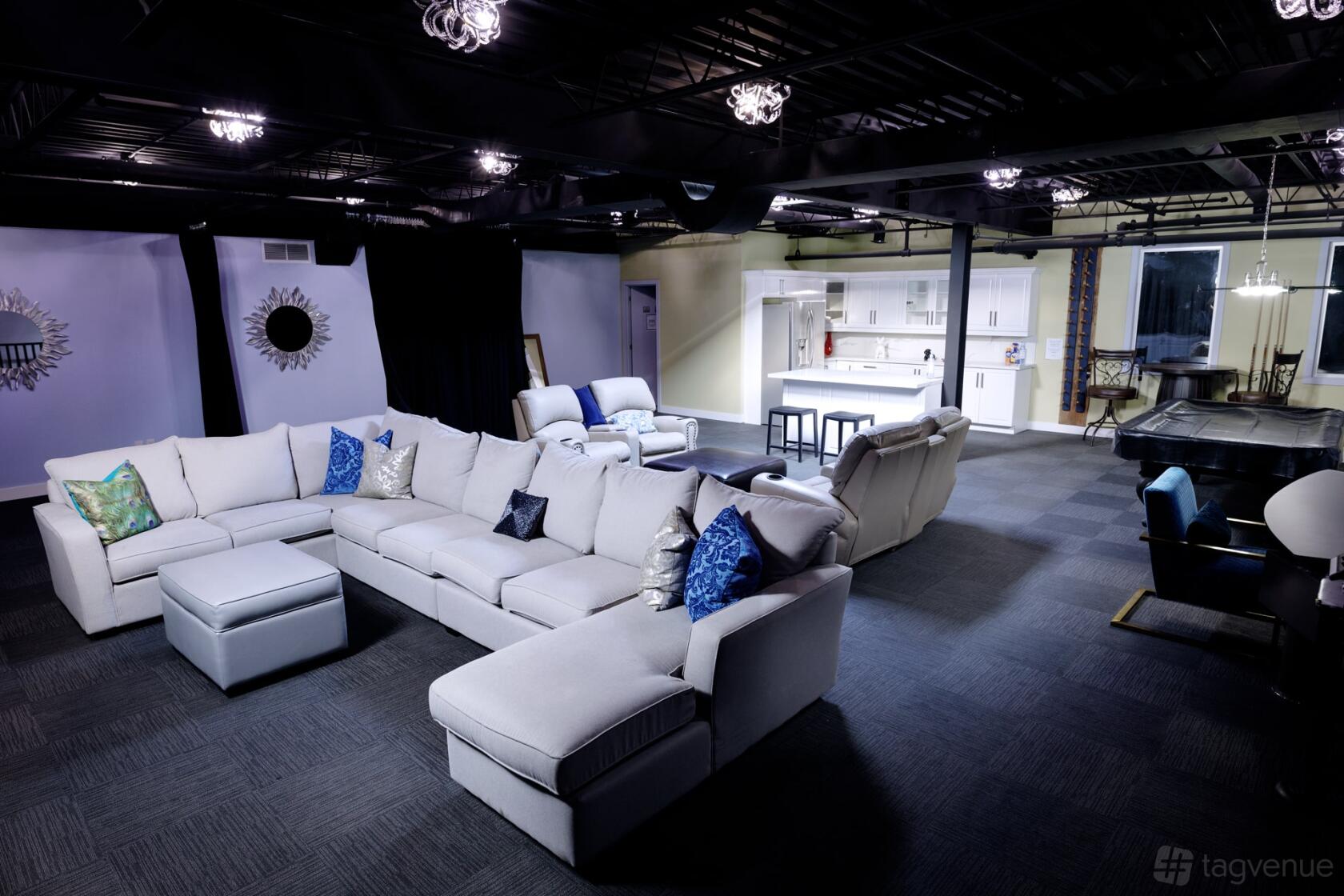 A film studio lounge with a large sectional sofa, accent chairs, and an open kitchen at MDC Music Studios.