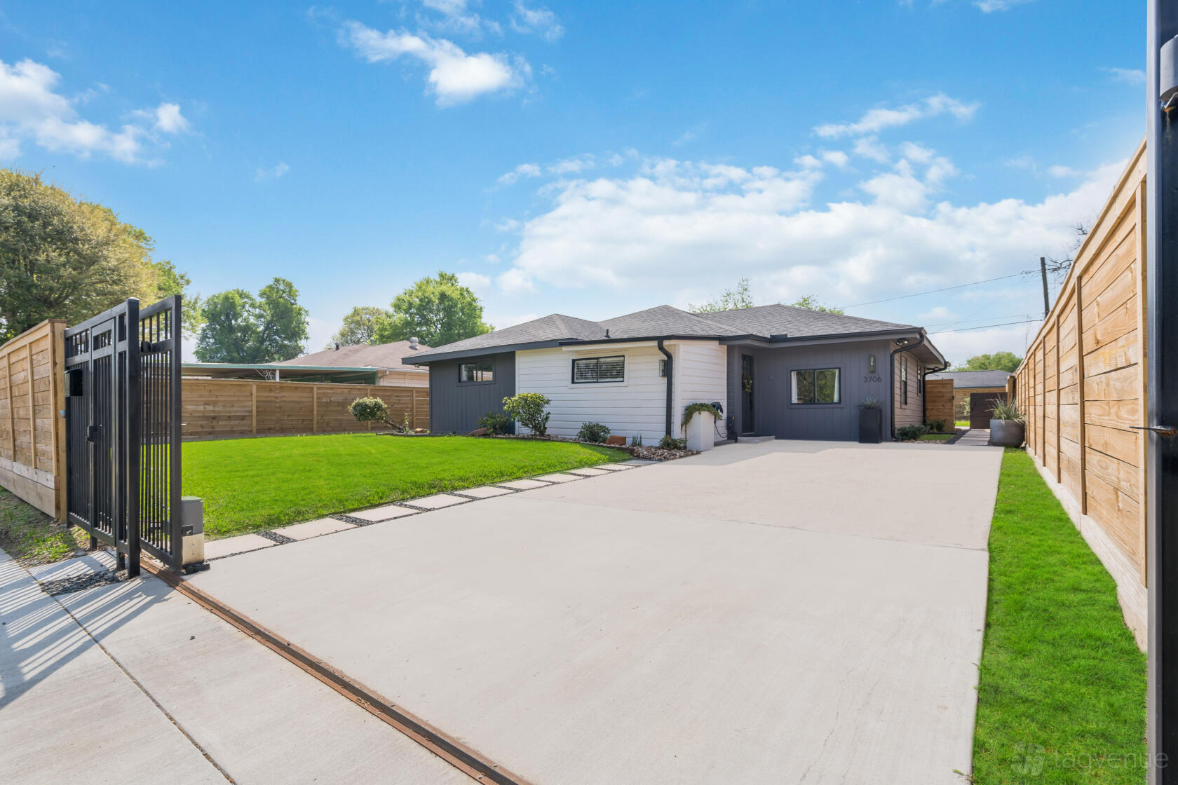 An apartment with a gated driveway, manicured lawn, and wooden privacy fencing at The Modern Haven Home.