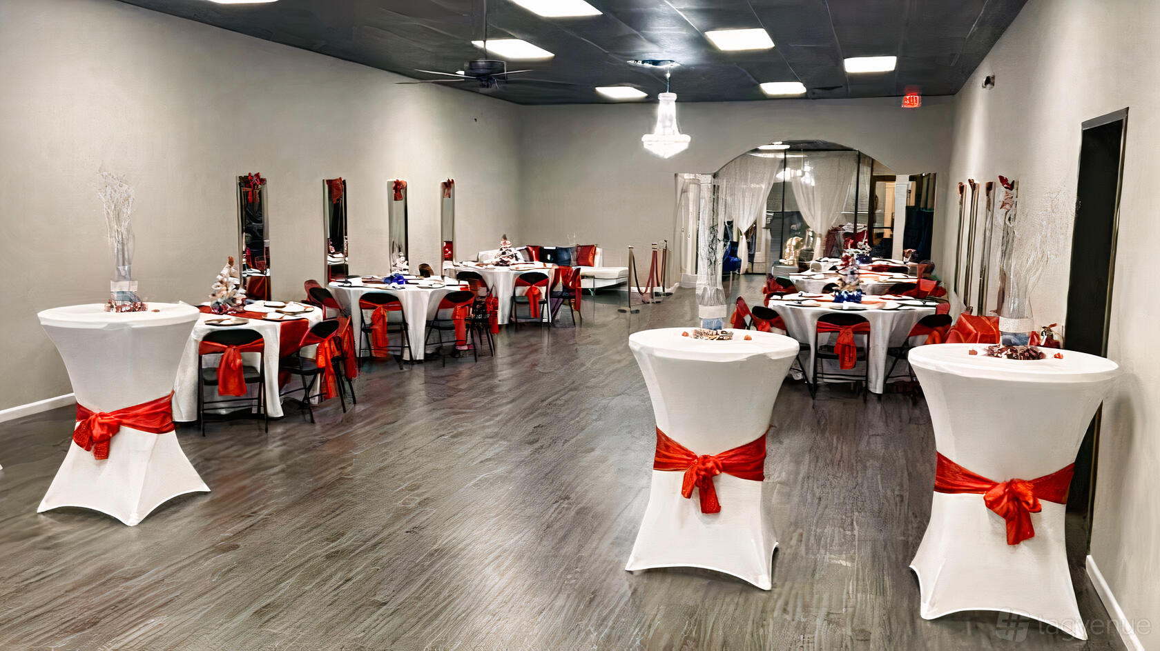 An event venue with cocktail tables and banquet tables draped in white linens and red sashes at 2xtra Events.